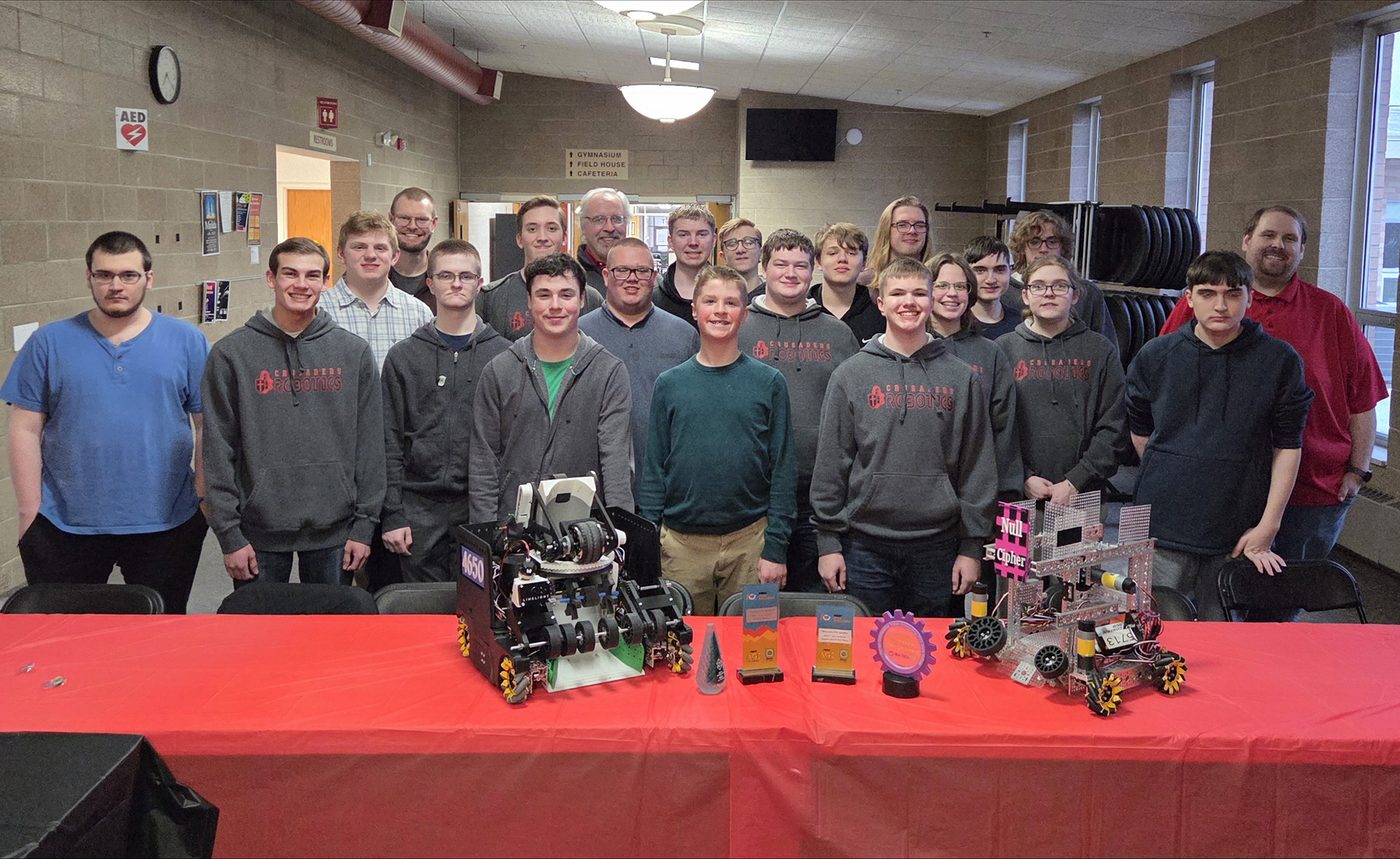 The whole Crusader Robotics program — about twenty students and their coaches — gathered behind their robots and trophies at the spring banquet
