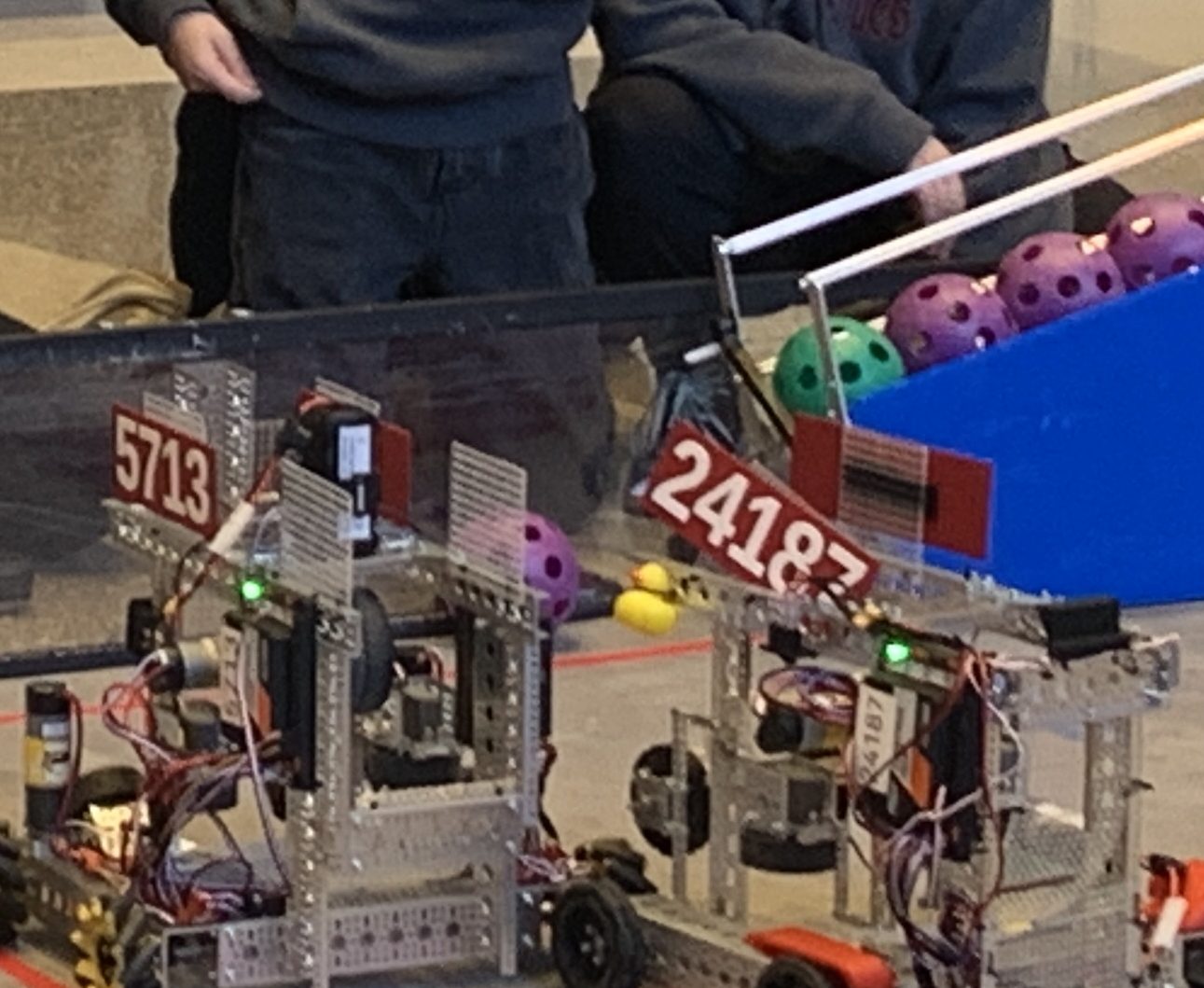 Team 24187's robot, labeled 24187, on the competition field next to teammate Team 5713's robot, with game artifacts in play