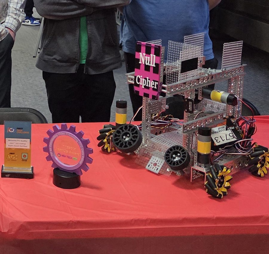 Team 5713's robot, Null Cipher, on the red banquet table — its pink nameplate, mecanum wheels, and the team's Inspire Award trophies alongside